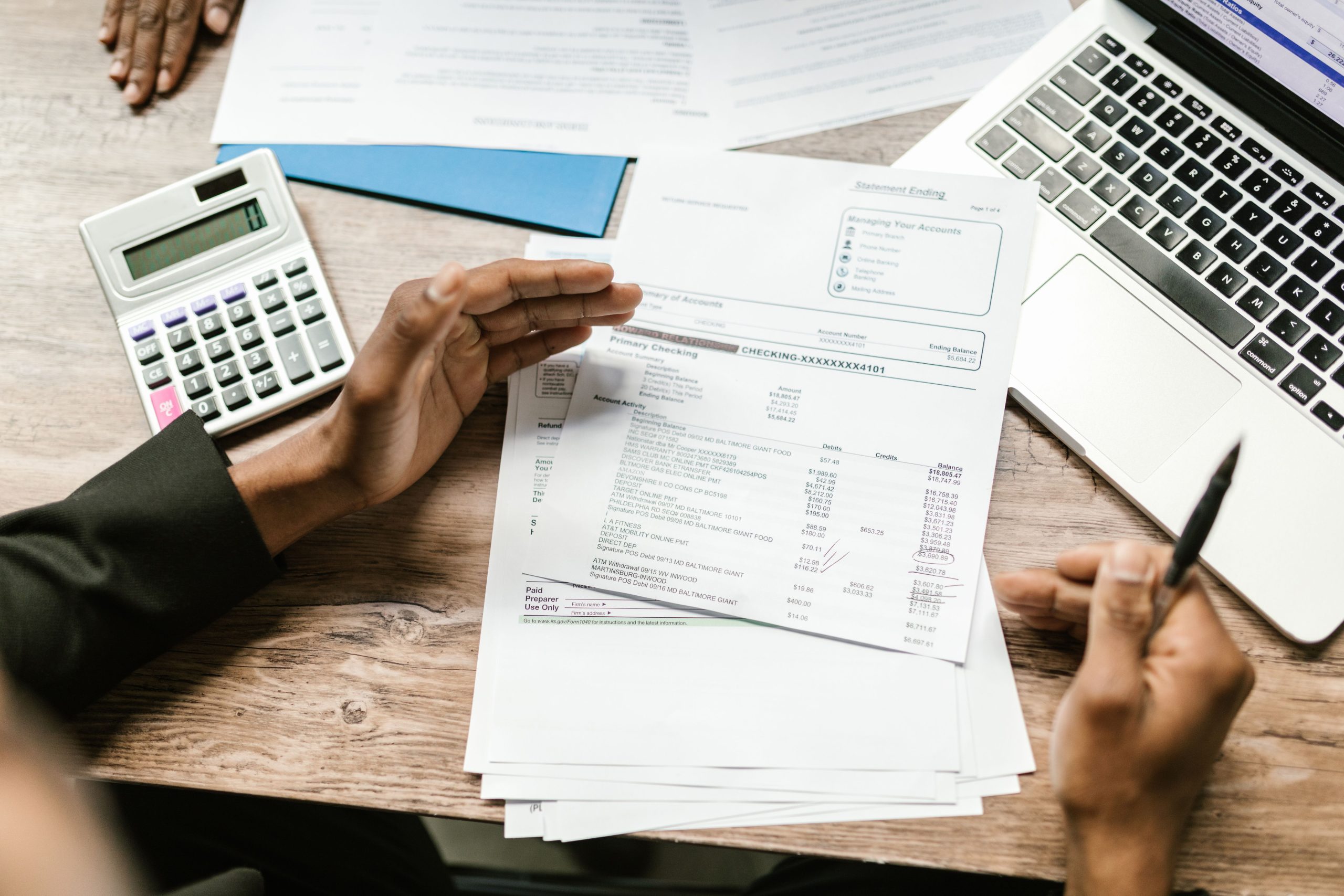 Hands holding financial documents with a calculator and laptop on an office desk