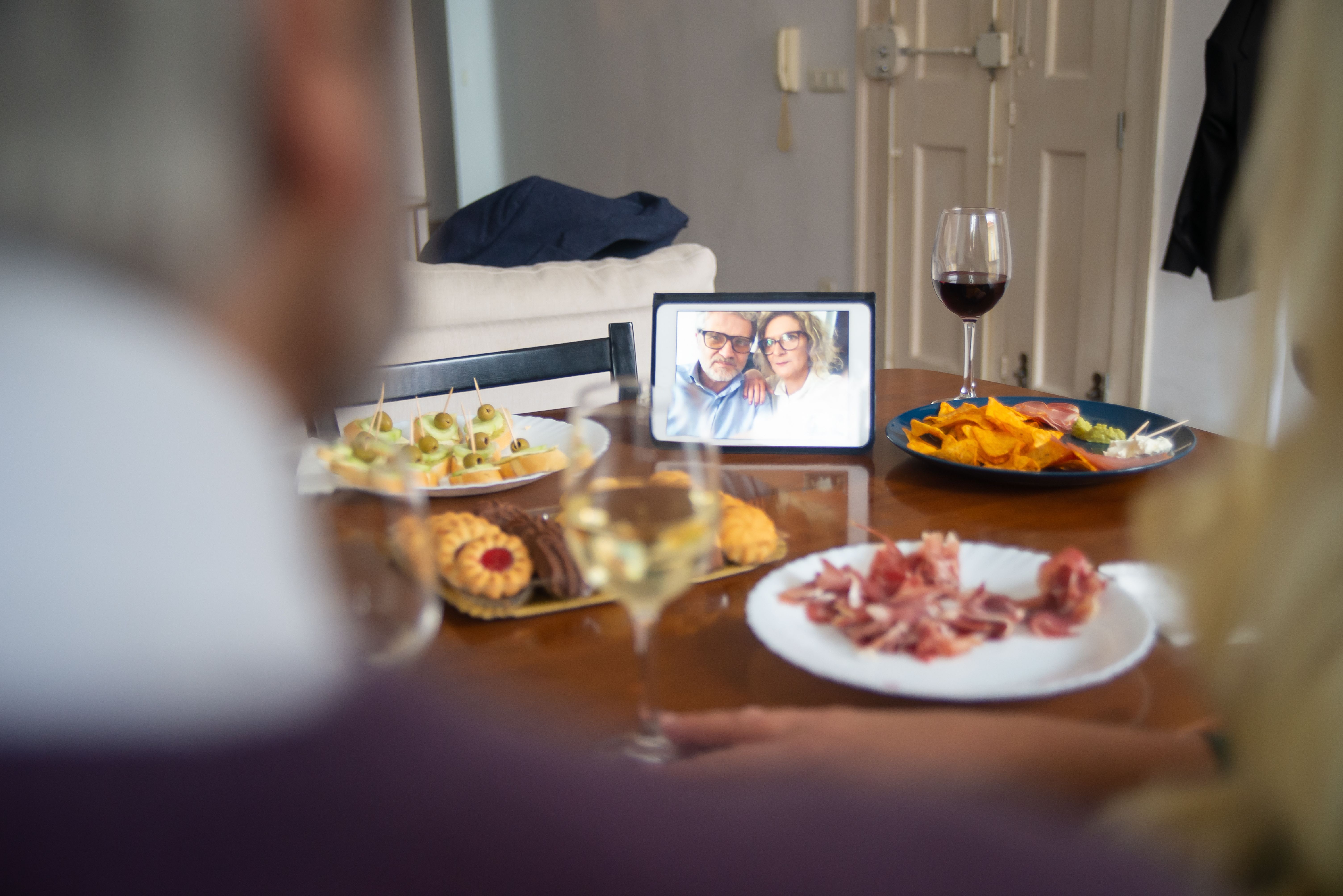 Couple sharing a meal while connecting with someone through a video call on a tablet.